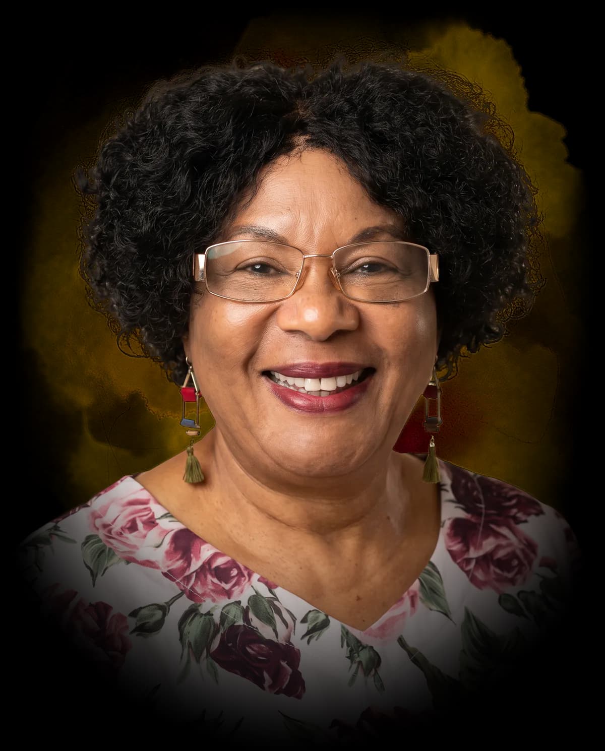 Junah Mpofu smiling, in gold-rimmed glasses, tasselled earrings and a rose-print blouse, against a gold watercolour wash.